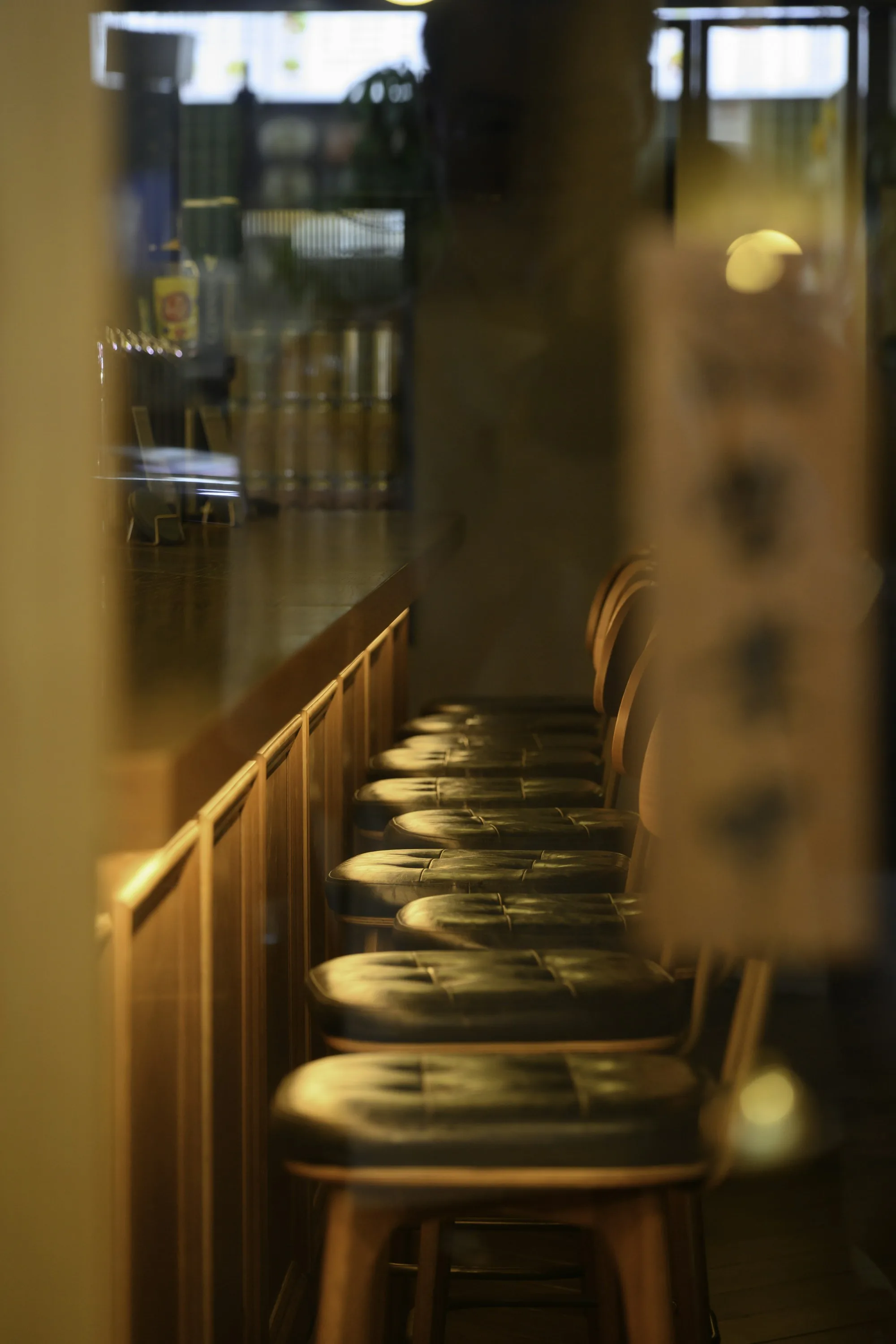 A row of empty bar stools in a warm-lit restaurant before service — the seat waiting for the new hire on Day 1